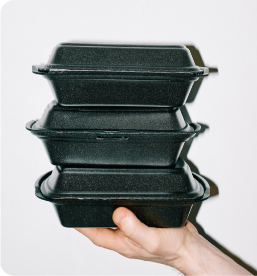 A hand shown holding 3 stacked black delivery containers often associated with containing food.